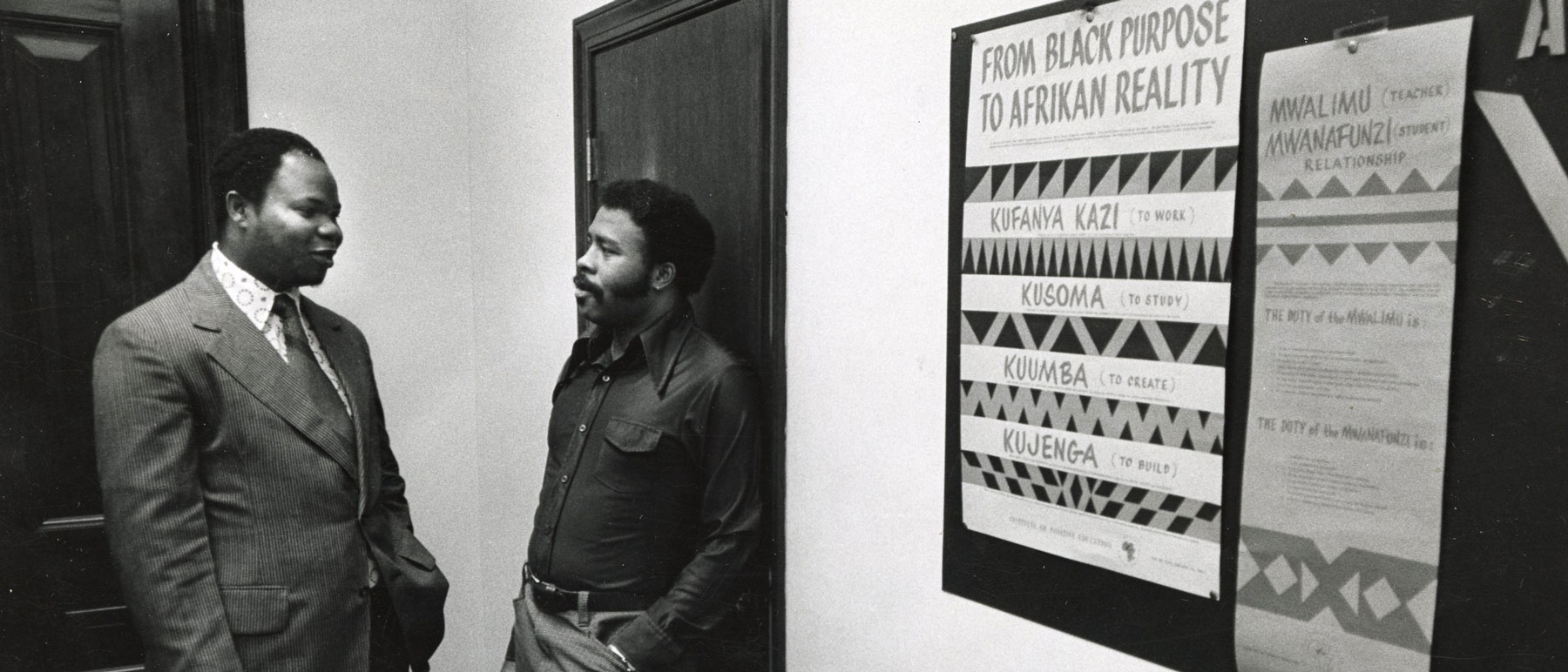 two v.c.u. professors from the 1970s have a hallway discussion in front of a poster titled 'from black purpose to afrikan reality'