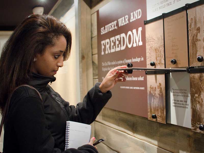 a student visitor to a museum interacting with an exhibit on slavery, war and freedom