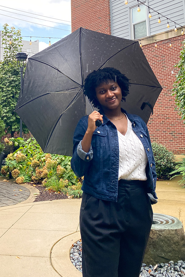 Dulanda Saintcyr stands outside in front of a brick building holding an umbrella
