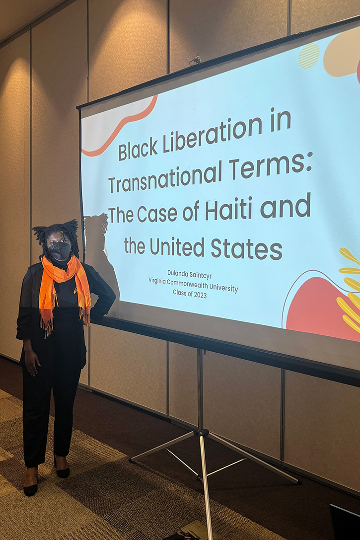Duland Saintcyr stands in front of a projector showing a presentation entitled 'Black Liberation in Transnational Terms: The Case of Haiti and the United States
