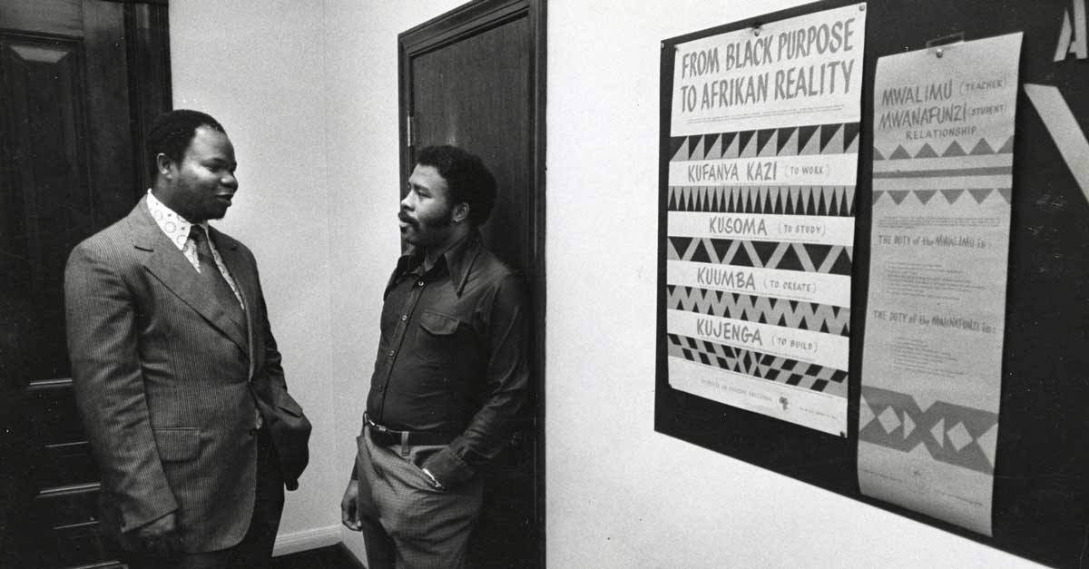 two v.c.u. professors from the 1970s have a hallway discussion in front of a poster titled 'from black purpose to afrikan reality'