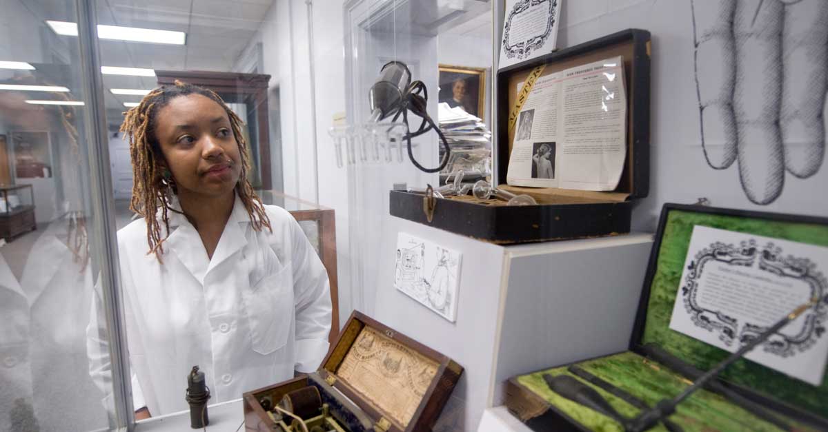 a student in a lab coat looking at a display case full of medical artifacts