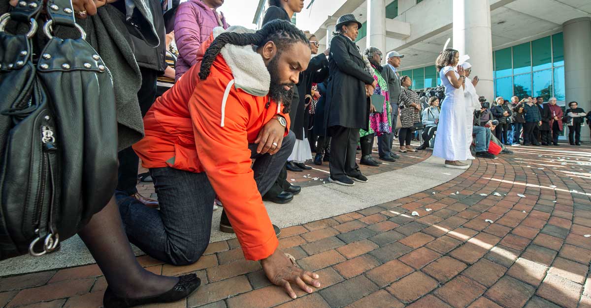 an attendee in reflection at an outdoor event commemorating the 19th-century human remains found in an M.C.V. Campus well