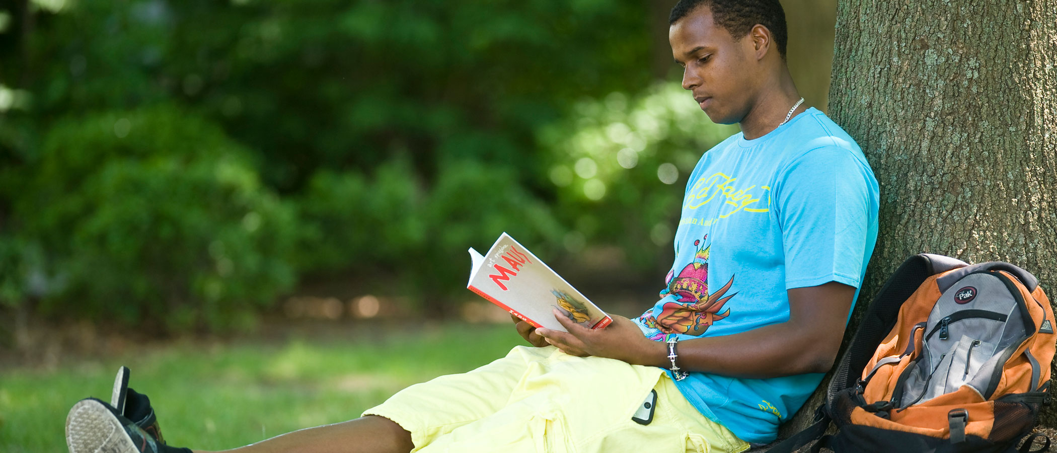 a v.c.u. student sitting under a tree reading a book